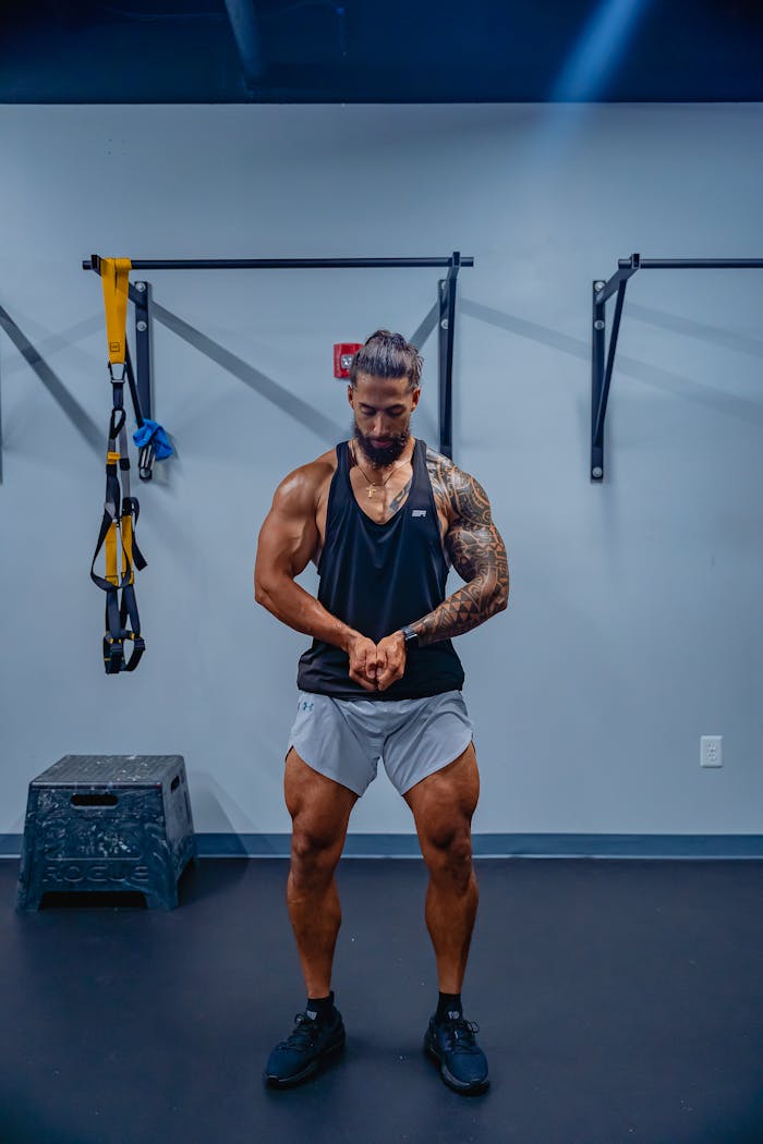 Tattooed bodybuilder flexing muscles in gym with gym equipment background.